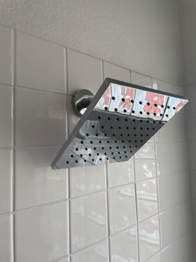 A brand new square-shaped shower head just installed on the wall in a shower
